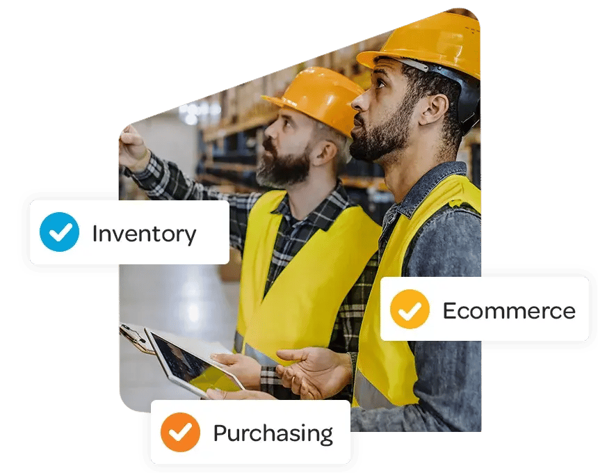 Two workers in a warehouse inspecting shelves, both wearing orange helmets and yellow vests