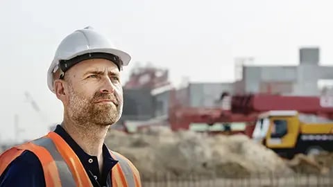 Man wearing a hard hat and orange safety vest looking upwards