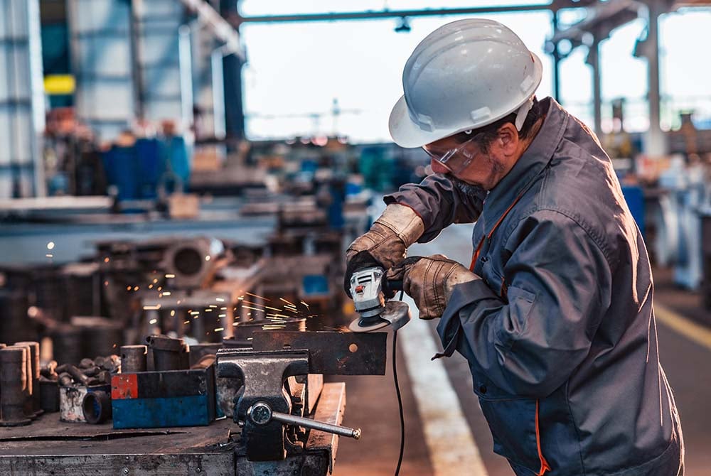 Side view of a factory worker operating a grinding machine in a metal industry workshop