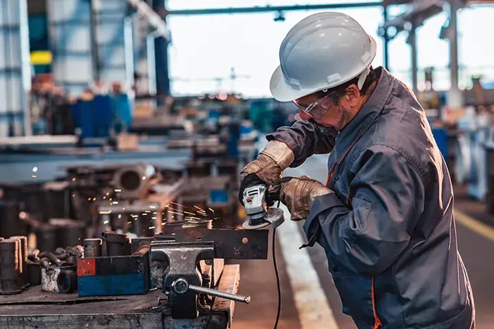 Side view of a factory worker operating a grinding machine in a metal industry workshop