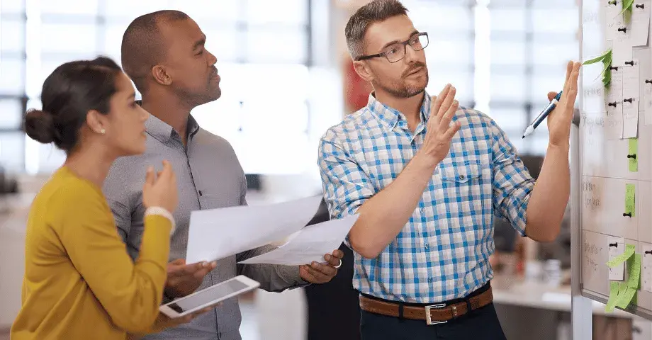 Three business professionals reviewing plans and discussing requirements during an ERP software evaluation meeting.